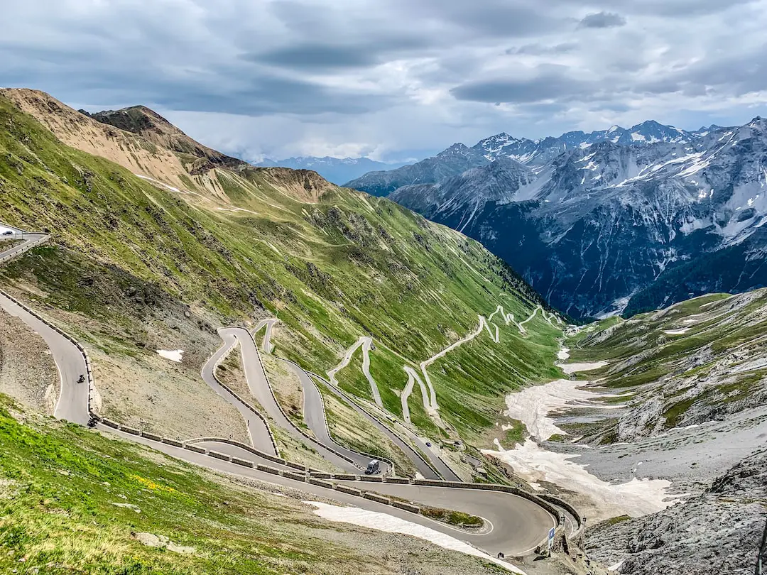 gray asphalt road between green mountains under gray cloudy sky during daytime