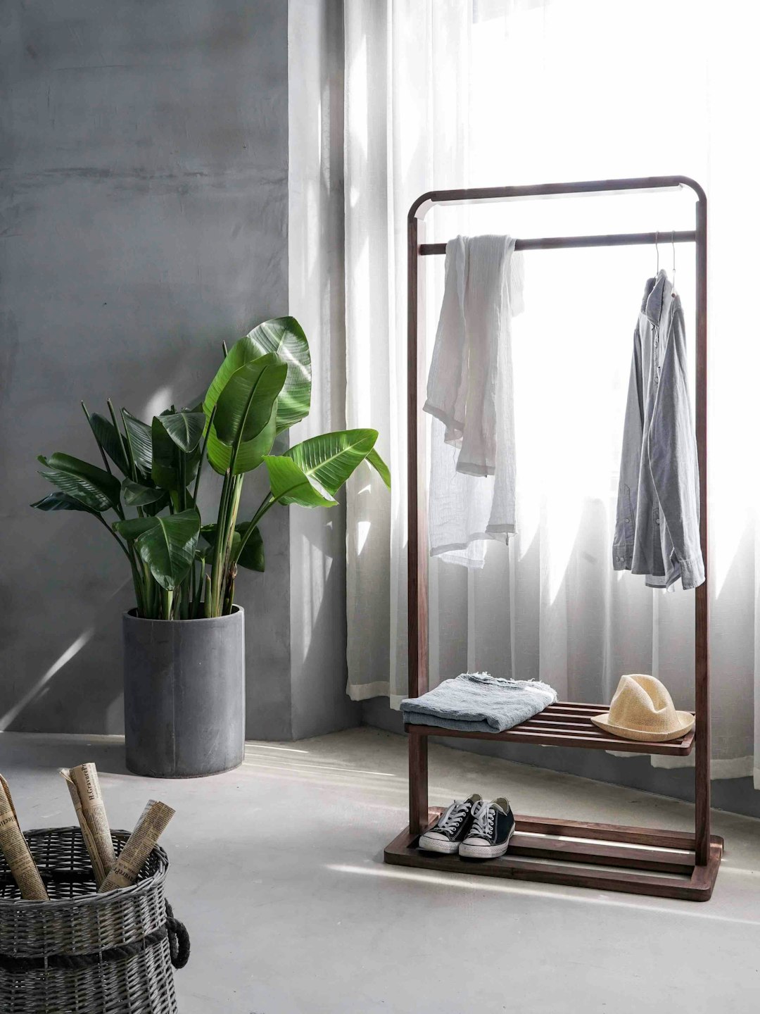 Tidy minimal interior by Case Brands gray dress shirt hang on brown wooden rack in front of window with white curtain