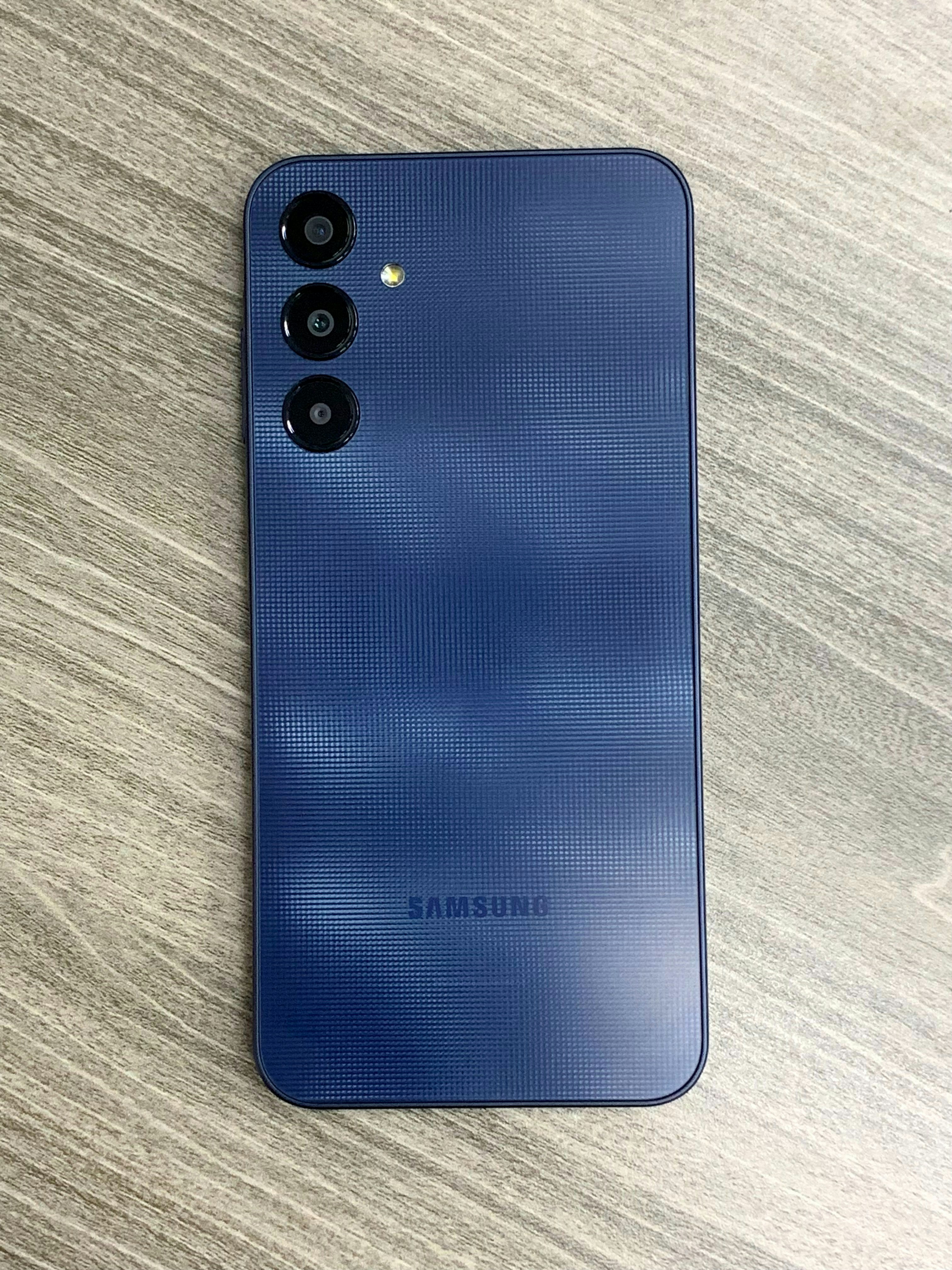 a blue samsung phone sitting on top of a wooden table